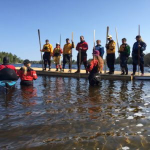 Students on a dock with kayak paddles learning how to teach kayak rolling.